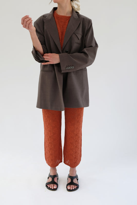 A model wearing a terracotta-colored, hand knitted floral cotton lace pant with a straight leg and gentle elastic waist.
