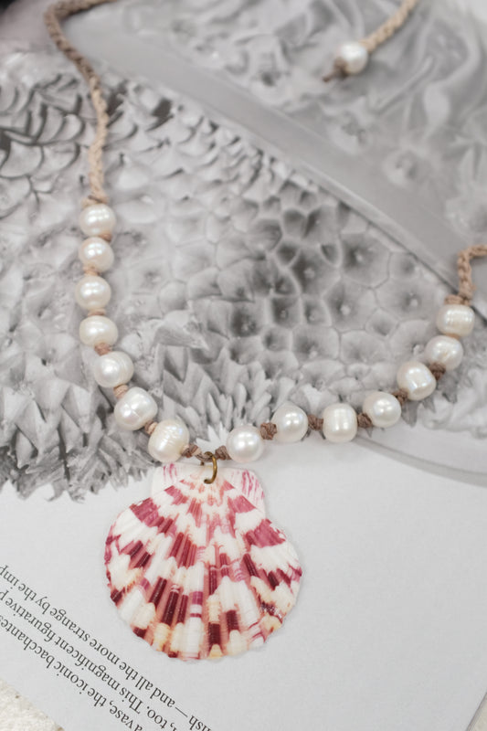 Pearl necklace on a textured surface with a pink object partially visible. Pearl & Shell Pendant Necklace