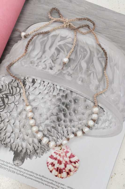 Pearl necklace on a textured surface with a pink object partially visible. Pearl & Shell Pendant Necklace